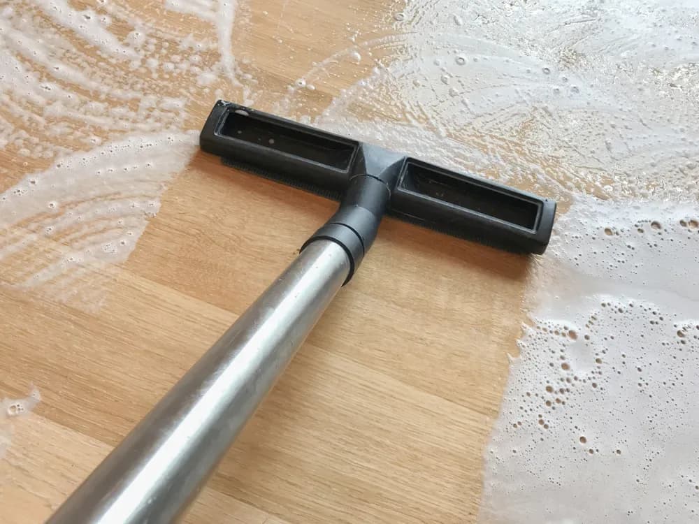 Cleaning wand scrubbing a wood floor with foam
